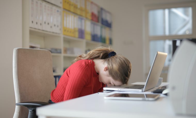 Een vrouw legt haar hoofd op haar laptop