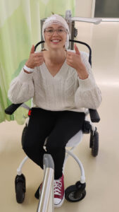 Je ziet Marlena in een rolstoel zitten met verband om haar hoofd.