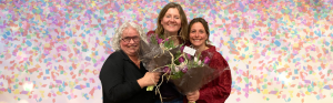 Drie vrouwen met stralende glimlach en bossen bloemen. Confetti op de achtergrond.