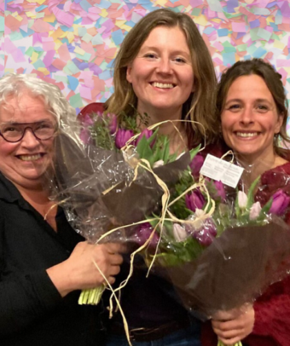 Drie vrouwen met stralende glimlach en bossen bloemen. Confetti op de achtergrond.