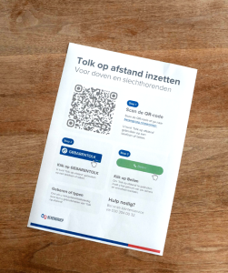 Poster op houten achtergrond, op de poster staat de tekst "Tolk op afstand"