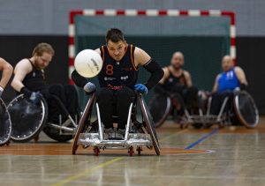 Man zit op rolstoel in sport kleding, bal rolt weg