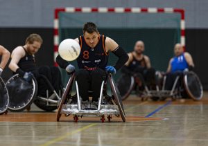 Man zit op rolstoel in sport kleding, bal rolt weg