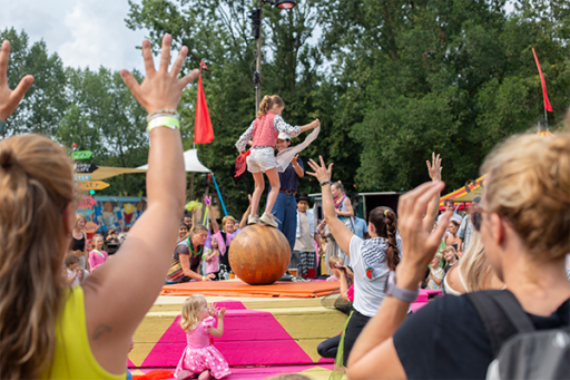 groep kinderen die juichen. podium met kind op en grote bal balancerend. Circus decor.
