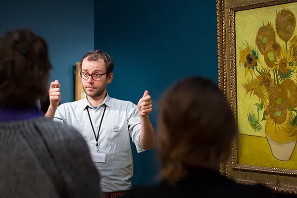 Tolk die rondleiding geeft naast schilderij van vincent van gogh met gele zonnebloemen