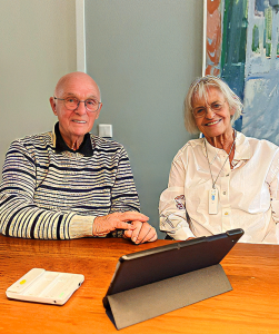 Bejaarde man en vrouw zitten aan tafel met een ipad voor hun