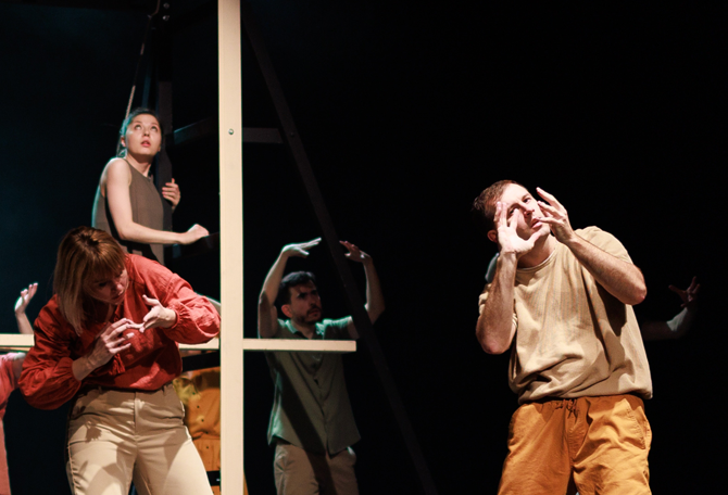 Groep mannen en vrouwen staan op podium en maken gebaren en spelen een theaterstuk