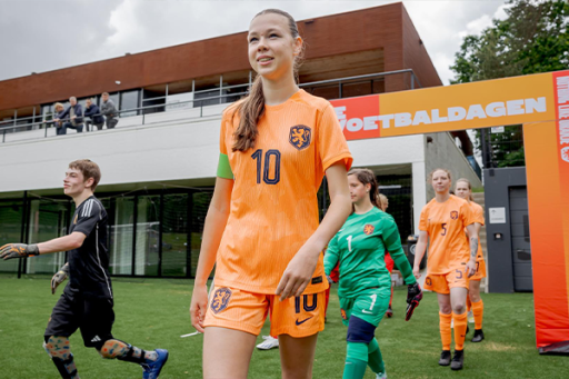 Jonge vrouw in voetbal kleding loopt voetbalveld op. ander voetbal spelers lopen achter haar.