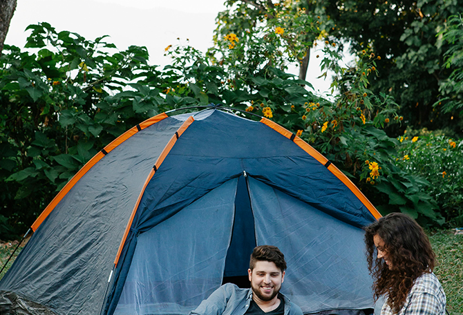 Blije man en vrouw zitten voor tent op de camping
