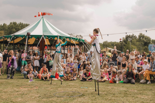 Twee meisjes op stelten gooien ringen over. Op de achtergrond een circustent.
